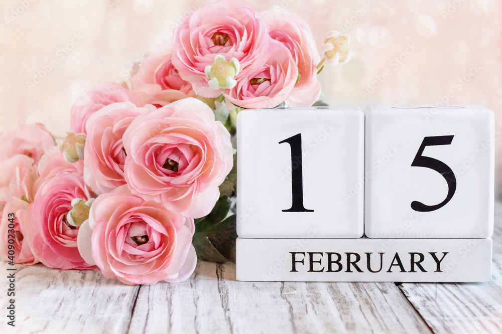 Fototapeta premium White wood calendar blocks with the date February 15th for International Childhood Cancer Awareness Day. Selective focus with pink ranunculus over a wooden table.