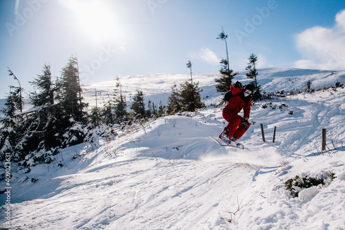 A guy in a red jumpsuit jumps on a snowboard from a snow ledge