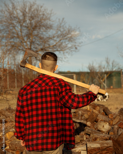 Guy lumberjack with axe in front of pile of woods.
