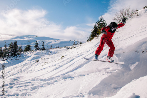 A guy in a red jumpsuit jumps on a snowboard from a snow ledge