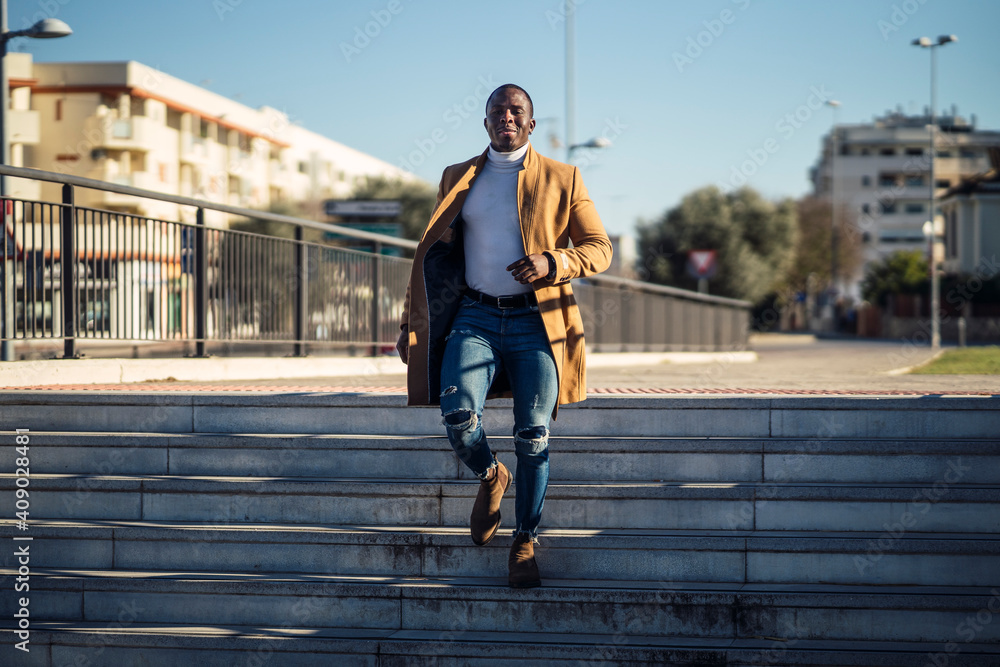 Chico negro atractivo posando con abrigo beige largo