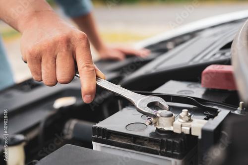 The hands of a skilled mechanic are holding a wrench to tighten a new car battery replacement nut, car care concept and to check battery health. And engine