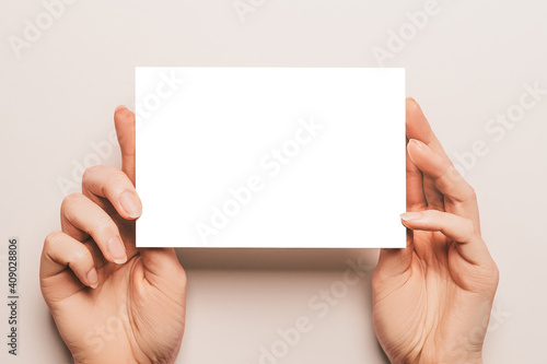 Fototapeta Naklejka Na Ścianę i Meble -  Female hands hold a blank sheet of paper on a beige background. Advertising space mock-up
