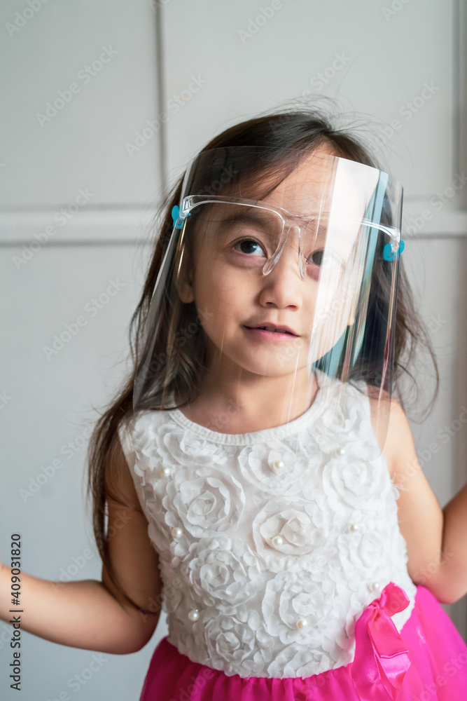 Naklejka premium A cute toddler girl wearing the face protection shield. A safety face shield corona mask during Covid-19 pandemic.
