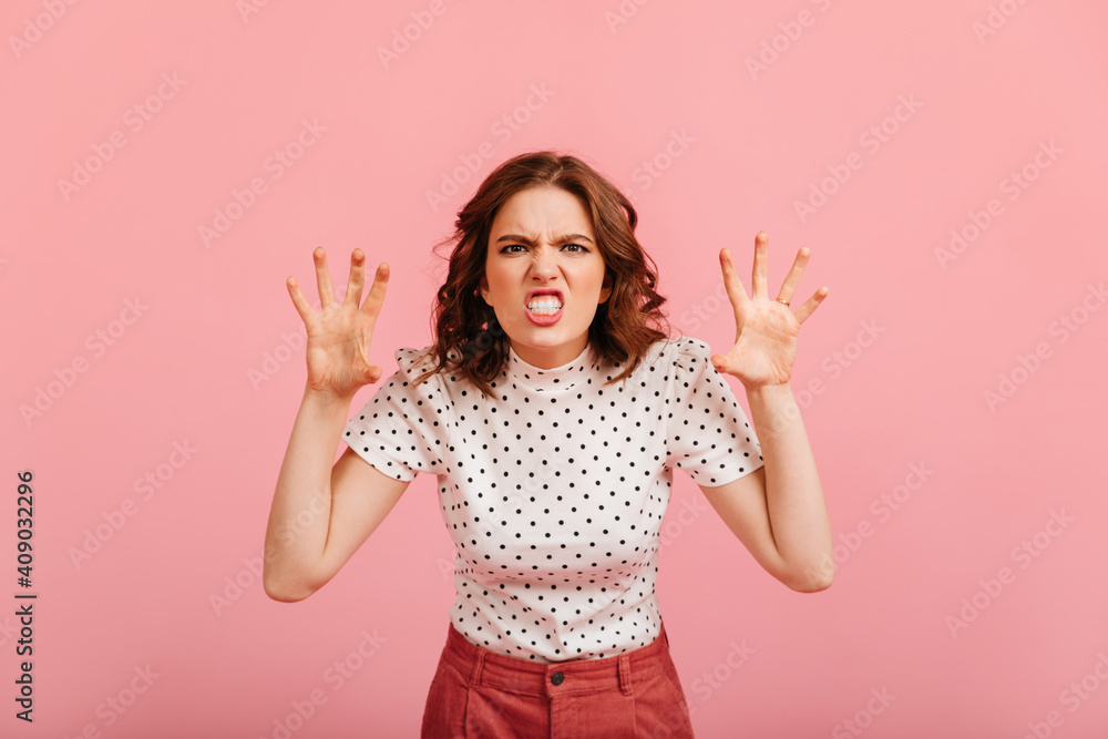 Aggressive girl making funny faces. Studio shot of angry lady in t-shirt isolated on pink background. Aggressive girl making funny faces. Studio shot of angry lady in t-shirt isolated on pink background.