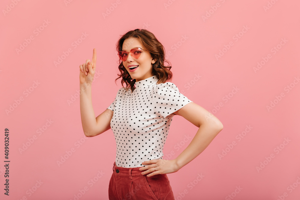 Glad curly woman posing in pink sunglasses. Studio shot of adorable girl in t-shirt. Glad curly woman posing in pink sunglasses. Studio shot of adorable girl in t-shirt.