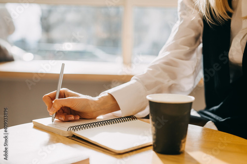Canvas Print Closeup of a woman sitting at a table with a cup of coffee, writing down ideas in a notebook
