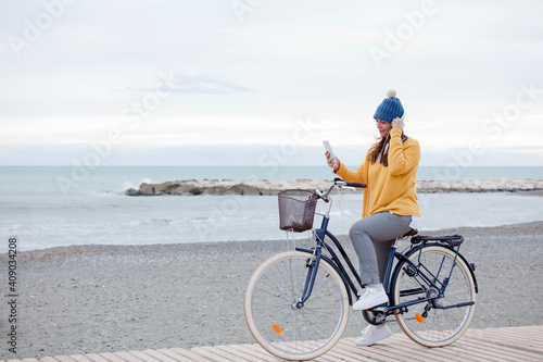 Beautiful active mature woman with bicycle on the road by the sea. Happy smiling middle aged woman with headphones listening to music, copy space © Fernando