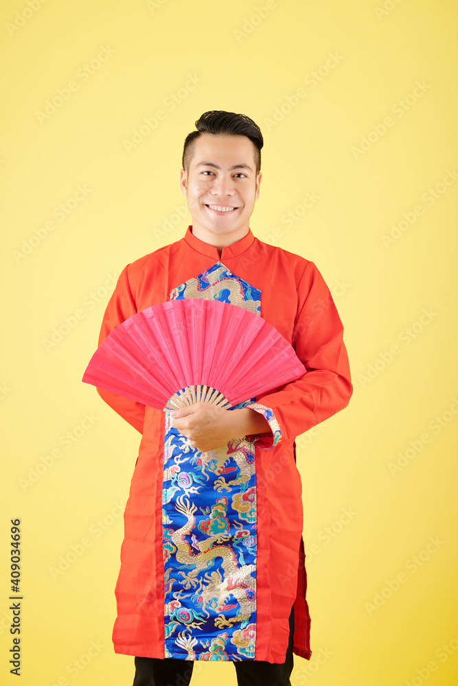 Portrait of happy young Asian man in traditional costume for Chinese New Year celebration posing with fan Portrait of happy young Asian man in traditional costume for Chinese New Year celebration posing with fan