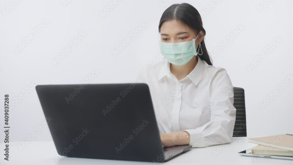 Young businesswoman on white office shirt wearing surgical mask while working on her computer at home during work from home COVID lockdown, filmed in slow motion on white background Young businesswoman on white office shirt wearing surgical mask while working on her computer at home during work from home COVID lockdown, filmed in slow motion on white background