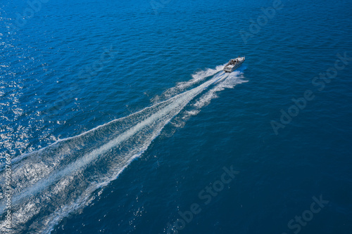 Top view of a white boat sailing in the blue sea. Drone view of a boat sailing at high speed. Aerial view of a boat in motion on blue water. luxury motor boat.