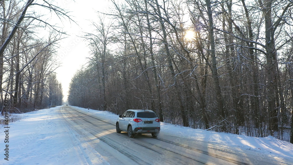 White car fast riding through snow covered icy road. SUV going at empty countryside route in winter forest on sunny day. Auto moving through scenic landscape way. Travel concept. Top view Drone shot White car fast riding through snow covered icy road. SUV going at empty countryside route in winter forest on sunny day. Auto moving through scenic landscape way. Travel concept. Top view Drone shot