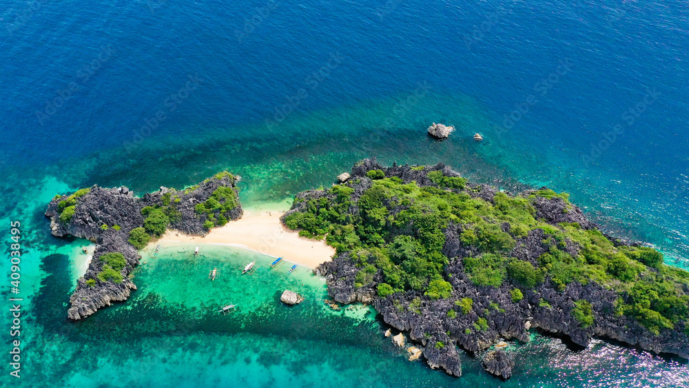 Aerial view of small isolated tropical island with white sandy beach and blue transparent water and coral reefs.