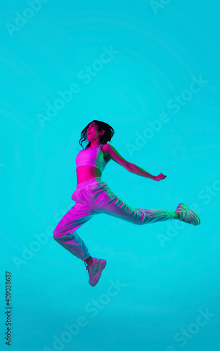 Free. Brunette woman's portrait on blue studio background in mixed neon. Beautiful model jumping high, flying with hair blowed out. Concept of human emotions, facial expression, sales, ad, fashion. © master1305