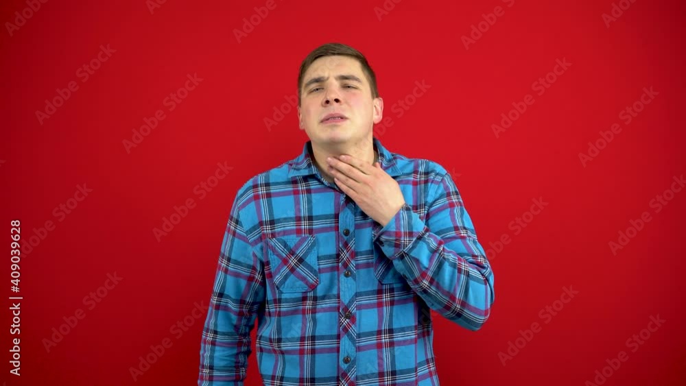 A young man has a sore throat and she touches him with his hand. Shooting on a red background. A young man has a sore throat and she touches him with his hand. Shooting on a red background.