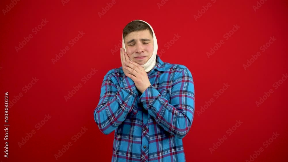 A young man has a rewound head due to a pain in a tooth. The man touches his cheek with his hand. Shooting on a red background. A young man has a rewound head due to a pain in a tooth. The man touches his cheek with his hand. Shooting on a red background.