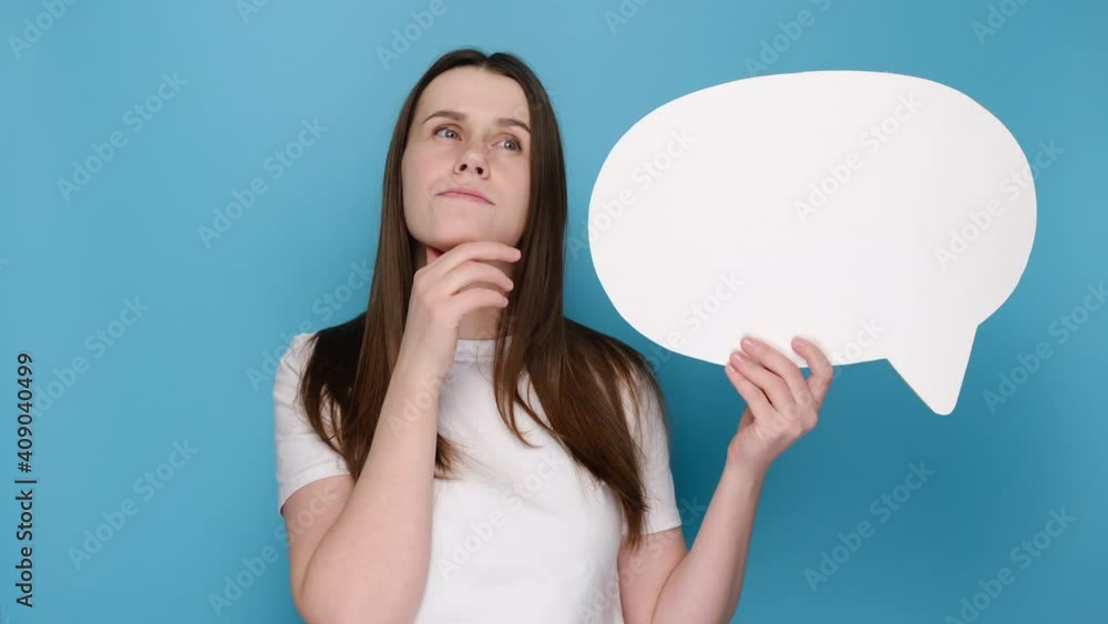 Portrait of worried pensive confused young woman holding empty speech bubble, spreading arms put hand prop up on chin, dressed in white t-shirt, isolated on blue wall studio. Emotion people concept Portrait of worried pensive confused young woman holding empty speech bubble, spreading arms put hand prop up on chin, dressed in white t-shirt, isolated on blue wall studio. Emotion people concept