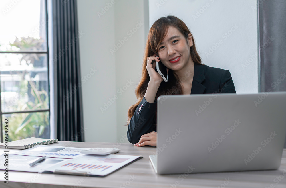 An Asian female finance worker sits on the phone with a customer who calls in to consult. At the office table, sit and work happily and smiling, concept over the phone. An Asian female finance worker sits on the phone with a customer who calls in to consult. At the office table, sit and work happily and smiling, concept over the phone.