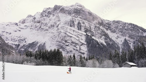 A Beautiful young woman is running in snowshoes with her golden retriever dog, in a white snow covered valley in the French Alps, The Criou is in the background. Haute-Savoie. photo