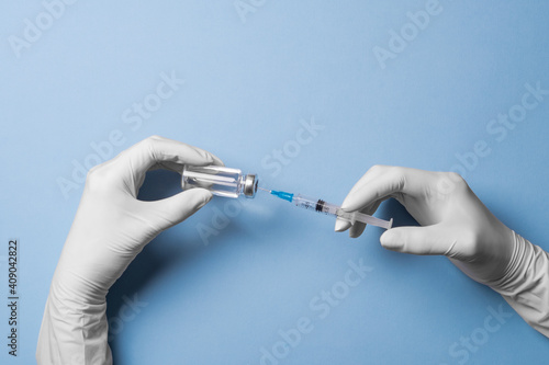 Doctor's Hand in white gloves hold the vial with vaccine or drug and syringe on blue background. The concept of protection against coronavirus infection, COVID-19. Banner