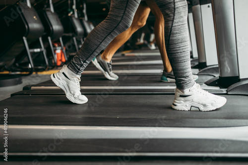 Young fit woman and man running on treadmill in modern fitness gym. Close up shot on moving legs.