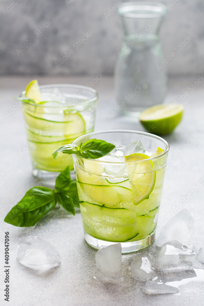 Refreshing summer homemade lemonade made from lime, lemon, cucumber and basil with ice in glass on old concrete background. Selective focus. Refreshing summer homemade lemonade made from lime, lemon, cucumber and basil with ice in glass on old concrete background. Selective focus.