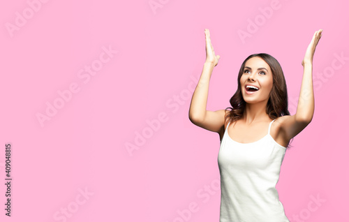 Obraz na plátne Portrait studio image of happy gesturing or praying young beautiful woman looking up, in white casual clothing, isolated over rose pink color background