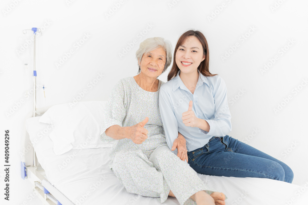 Obraz premium old asian patient sick and admit in hospital, young asian female visiting old female, they show thumbs up sign with hands, they feeling happy and smile in mother's day, elderly healthcare