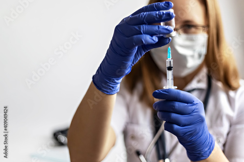 A female doctor wearing a medical mask draws the coronavirus vaccine into a syringe at the clinic.The concept of vaccination  immunization  prevention against Covid-19.