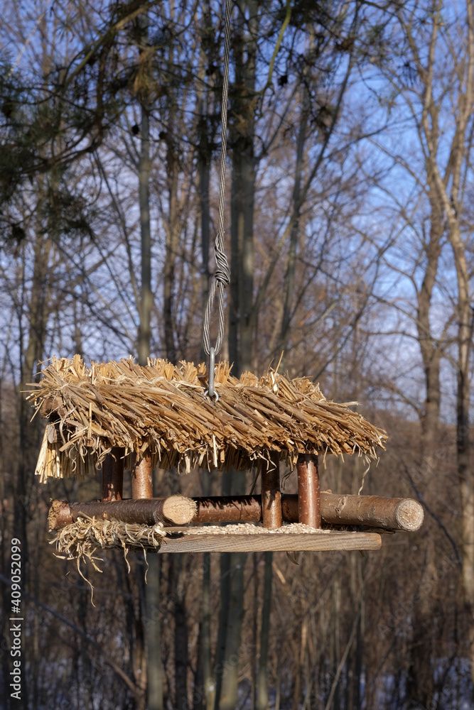 Hanging bird feeder with thatched roof, illuminated by the sun on a winter day Hanging bird feeder with thatched roof, illuminated by the sun on a winter day