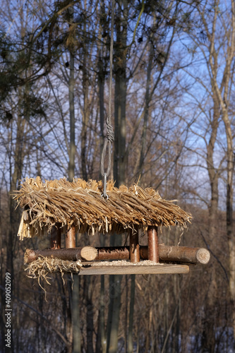 Hanging bird feeder with thatched roof, illuminated by the sun on a winter day