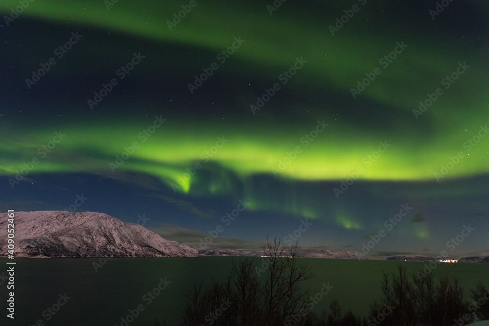 A massive aurora borealis show over a calm fjord in Alta