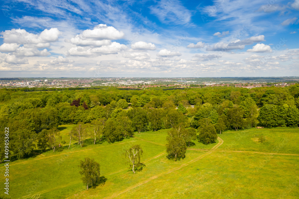 Obraz premium Aerial photo of the city of Leeds viewed from the village of Middleton and Middleton Park on a sunny day with white clouds in the sky and a lot of green trees in the summer time