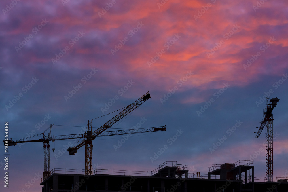 Some cranes and buildings with orange background Some cranes and buildings with orange background