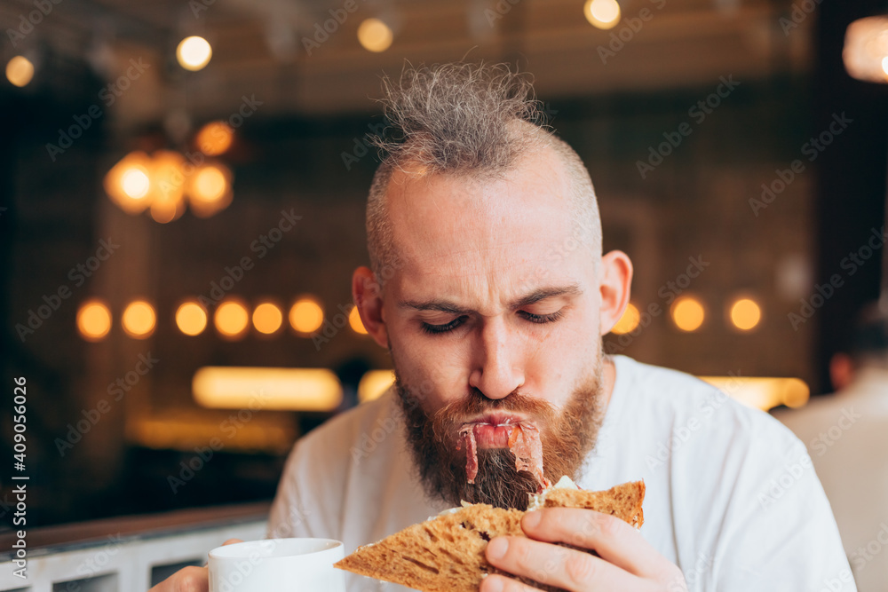 A brutal man of European appearance in a cafe has a delicious sandwich A brutal man of European appearance in a cafe has a delicious sandwich