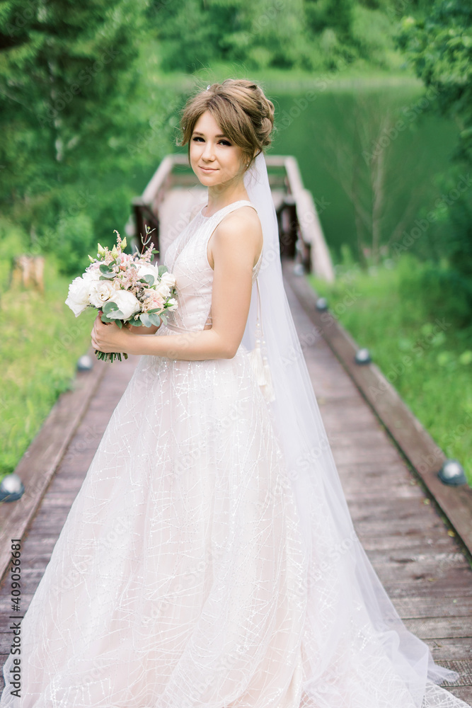 Beautiful bride in pink wedding dress. Outdoor romantic portrait of attractive brunette woman with flowers and hairstyle in prom dress with tulle skirt posing by nature
