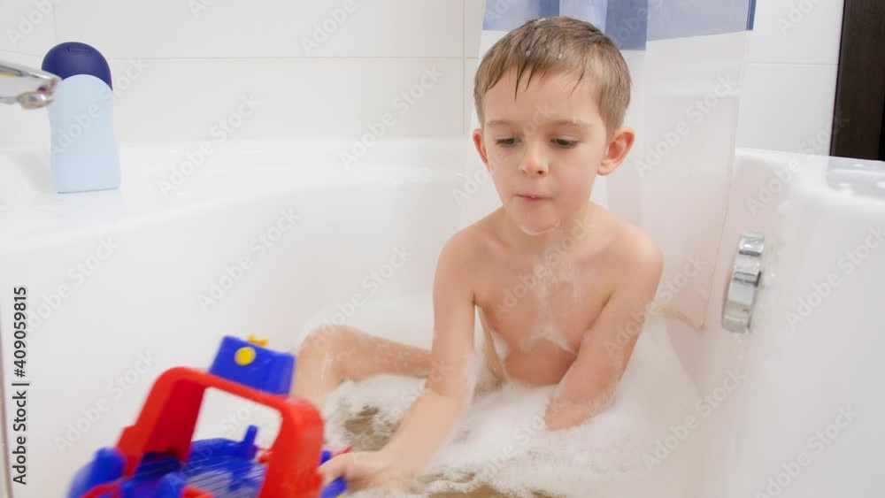 Cute little boy taking bath at home and playing iwth colorful toy ship or boat. Concept of child hygiene and health care at home. Kids having fun and playing Cute little boy taking bath at home and playing iwth colorful toy ship or boat. Concept of child hygiene and health care at home. Kids having fun and playing