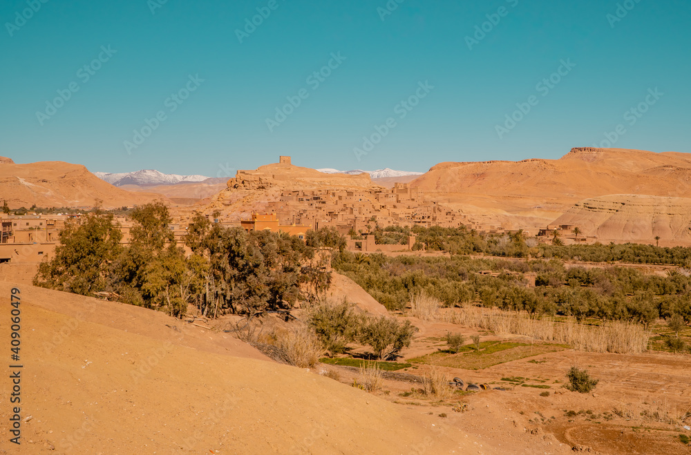 Panorama view of clay houses and the Kasbah (fortress) in the ancient town of Aid Benhaddou, Morocco with Atlas mountains in the background Panorama view of clay houses and the Kasbah (fortress) in the ancient town of Aid Benhaddou, Morocco with Atlas mountains in the background