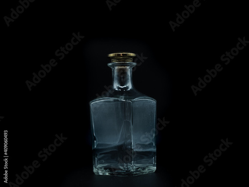 Empty glass bottle closed with big golden round cork isolated on a black background. Transparent square bottle. Front view of the vertical staying jar.