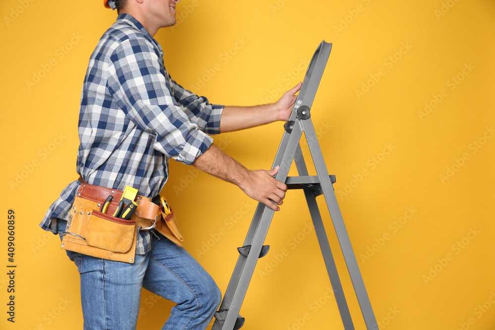 Professional builder climbing up metal ladder on yellow background, closeup Professional builder climbing up metal ladder on yellow background, closeup