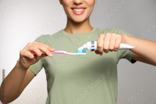 Woman applying toothpaste on brush against light background, closeup