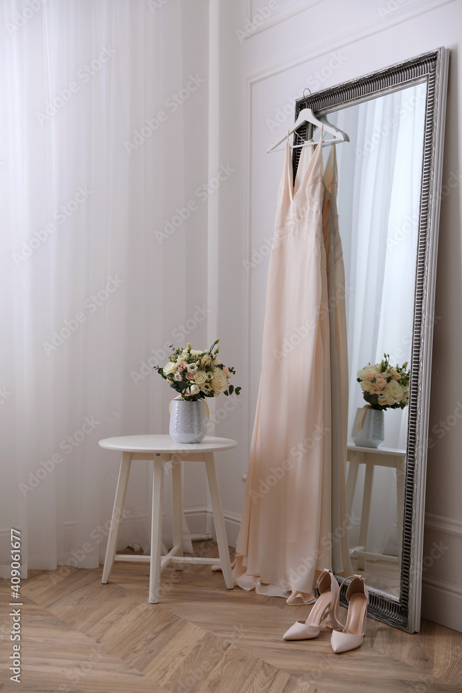 Elegant wedding dress hanging on large mirror in room Elegant wedding dress hanging on large mirror in room