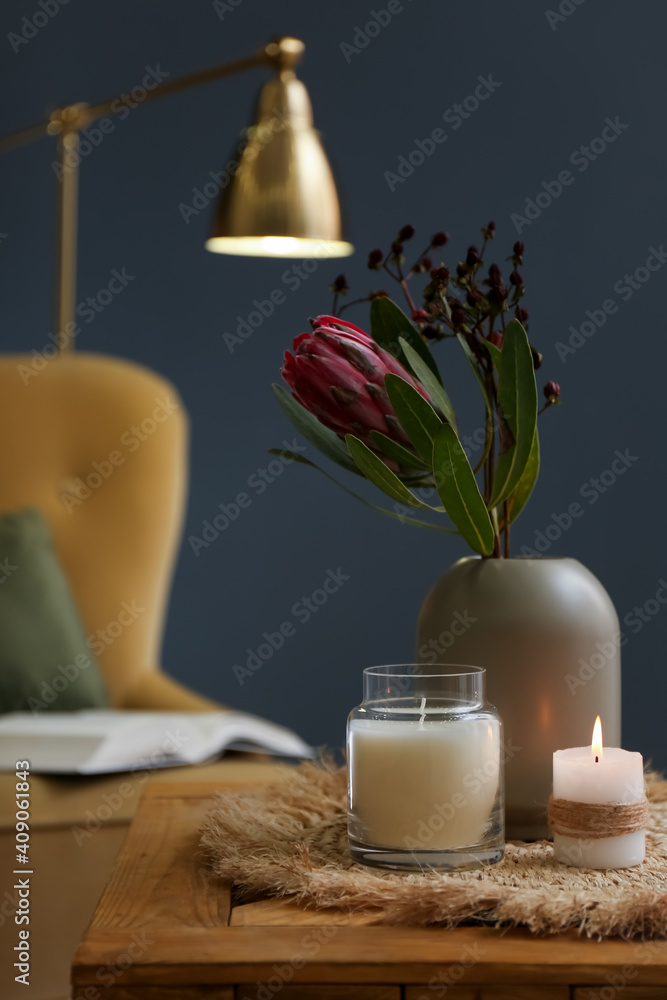 Vase with beautiful protea flowers and candles on wooden table indoors. Interior elements