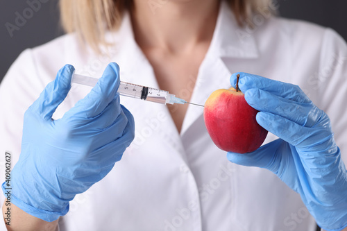 Woman scientist in rubber gloves making injection into apple closeup photo