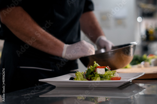 chef cook hands in gloves prepare or put healthy greek salad on plate at kitchen