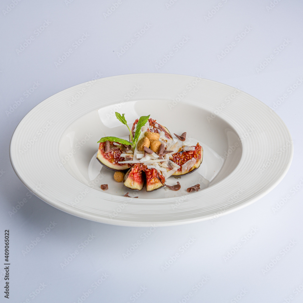 White plate with a fig or breva divided into four pieces decorated with coconut and mint, delicious combination of color and texture in a sweet dessert