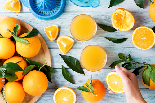 Fototapeta Naklejka Na Ścianę i Meble -  Two glasses of fresh juice, fruit squeezer and ripe fresh oranges on blue wooden table top, fresh orange juice making, top view