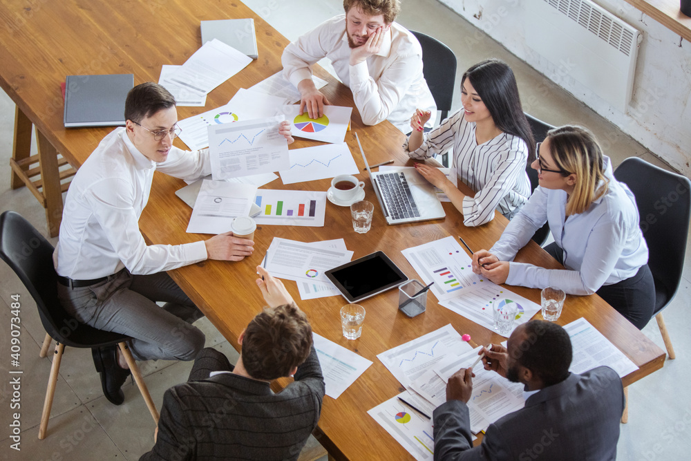 Top view. Diverse group of co-workers having casual discussion in office. Executives during friendly discussion, month reporting, creative meeting. Concept of business, finance, occupation, job. Top view. Diverse group of co-workers having casual discussion in office. Executives during friendly discussion, month reporting, creative meeting. Concept of business, finance, occupation, job.
