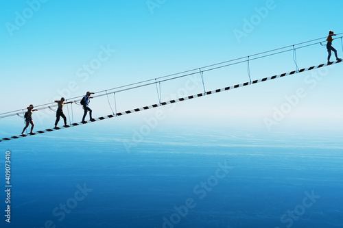 A suspension bridge over a cliff on the background of the sky with people climbing up.