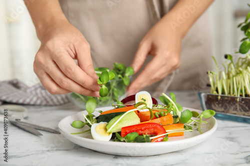 Woman making salad with fresh organic microgreen at white marble table, closeup